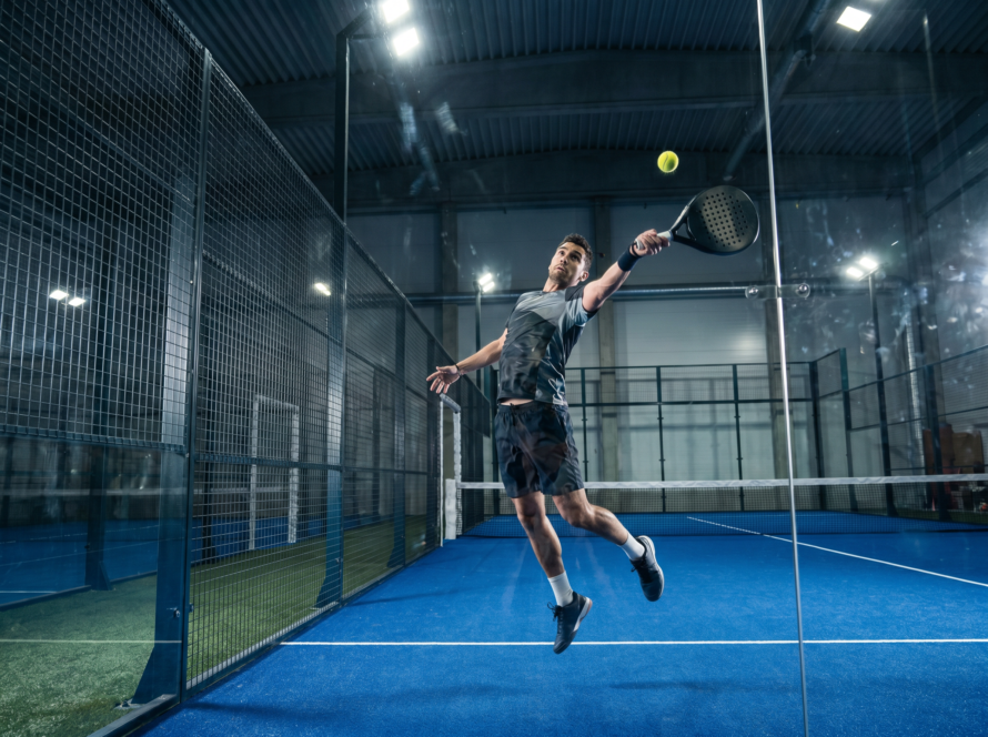 Padel player jumping to play a bajada off the back glass wall
