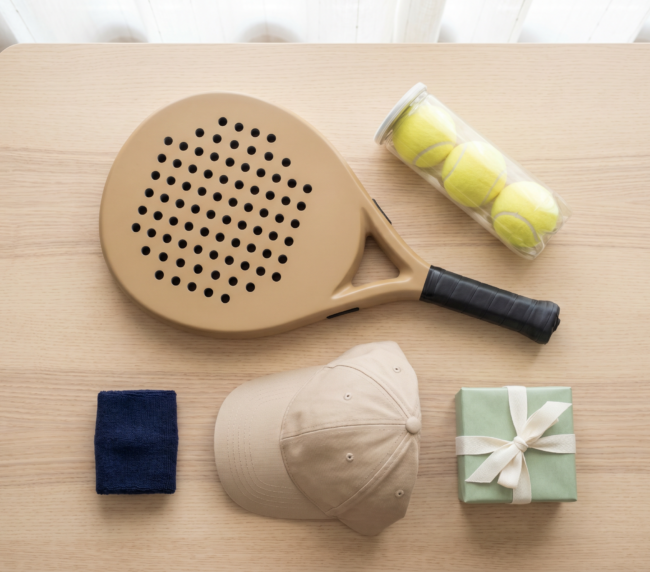 Padel gift ideas flat-lay: a padel racket, balls, cap and wristband with a gift box
