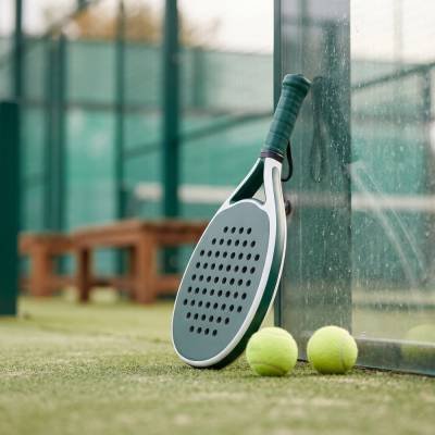 Padel bat leaning against court glass beside two balls