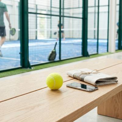 Padel ball, newspaper and phone on a bench beside a padel court